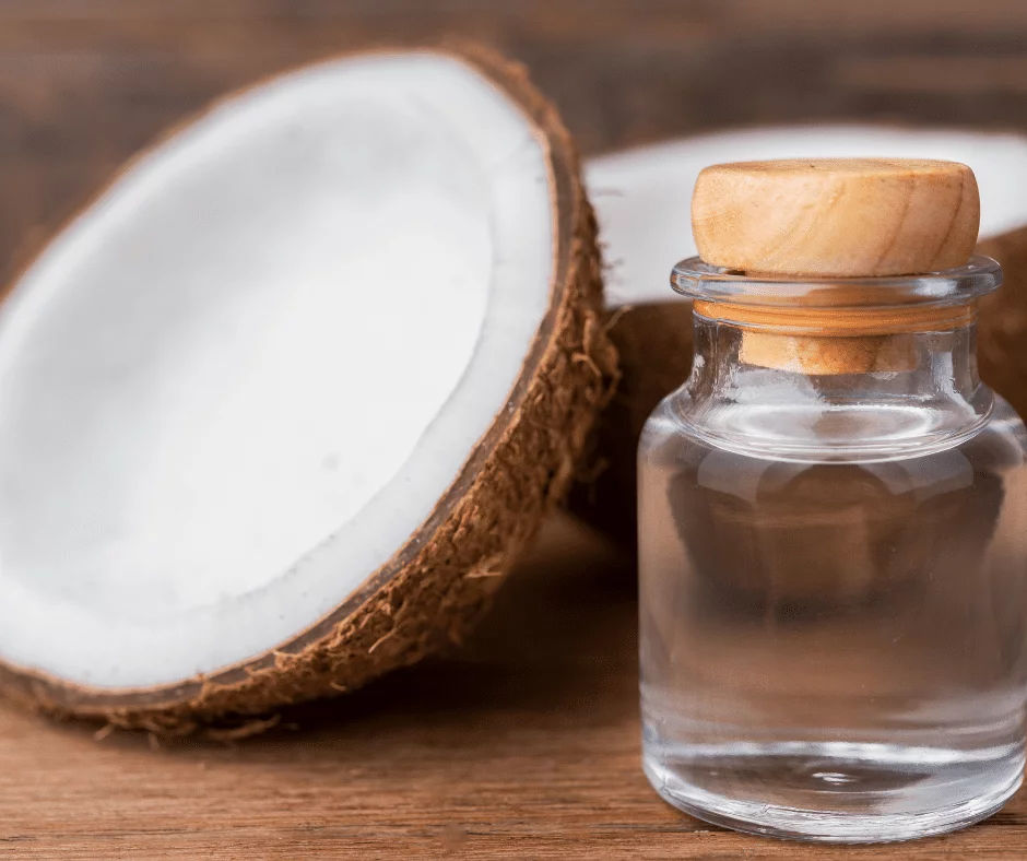 MCT oil in small glas bottle with wooden lid, in the backround to coconut halves on wooden table