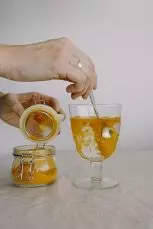 Two hands are preparing a Kurkuma drink using powder and a cup of water