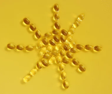 Vitamin D3 K2 Kapseln in Sonnenform auf gelben Hintergrund