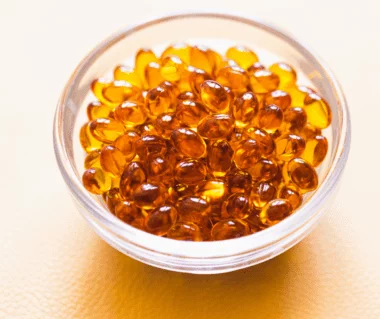Eine Glasschale mit Vitamin D3 K2 Kapslen auf einem orangenen Hintergrund