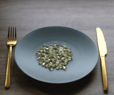 Vitamin D3 K2 auf einem grauen matten Teller mit goldenem Besteck auf einem grauen Holztisch