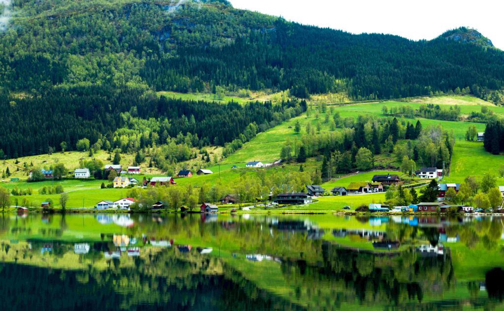 Skandinavische Landschaft mit Fjörd, Bergen und Wäldern. Vereinzelte Häuser sind zu sehen. 